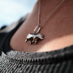 Load image into Gallery viewer, A close-up lifestyle shot of a person wearing a silver rhino pendant necklace on a delicate chain, styled with a dark gray knit top.
