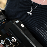 Load image into Gallery viewer, A close-up lifestyle shot of a person wearing a silver rhino pendant necklace over a black ribbed knit top, with a vintage black camera and lens partially visible in the foreground.
