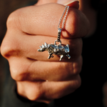 Load image into Gallery viewer, A close-up of a hand holding a silver necklace with a silver rhino pendant against a dark background.
