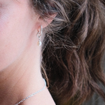 Load image into Gallery viewer, A close-up of a person's ear wearing a delicate silver hoop earring with a small white pearl drop, alongside a matching silver chain necklace.
