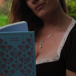 Load image into Gallery viewer, A close-up lifestyle shot of a woman wearing a delicate silver chain necklace with a single white pearl pendant, holding an open book with a blue floral cover.
