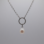 Load image into Gallery viewer, A silver chain necklace featuring a textured circular ring pendant with a dangling white pearl, set against a solid gray background.
