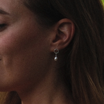 Load image into Gallery viewer, A close-up side profile of a woman wearing a small silver hoop earring with a dangling pearl drop.
